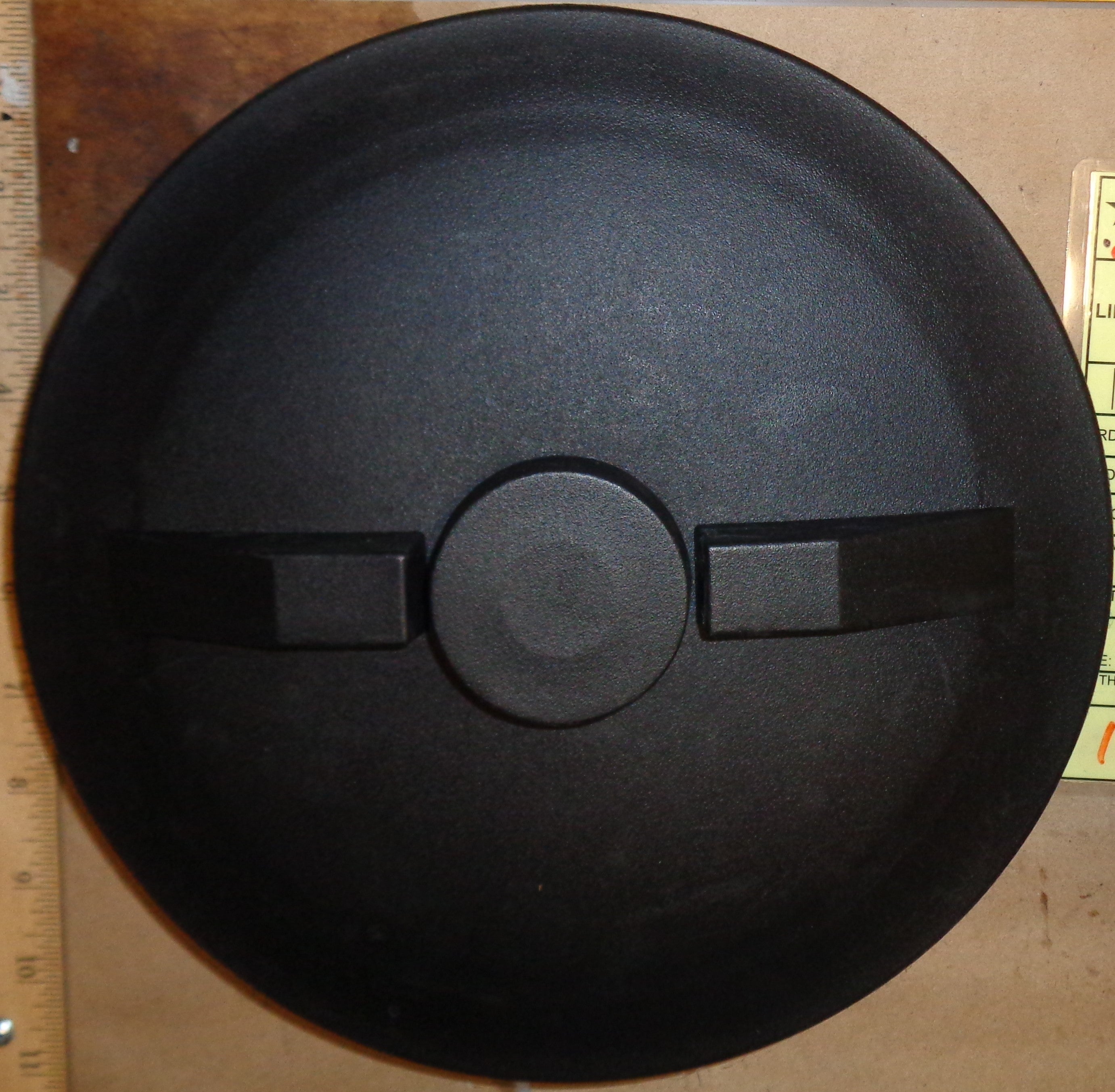 Black round object with a central circular feature on a wooden surface